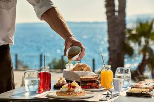 a table with food on it with a person pouring food at Poseidon of Paros Hotel & Spa in Chrissi Akti