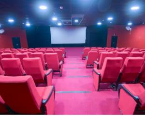 an empty auditorium with red chairs and a white screen at Hotel Rongla in Pālampur