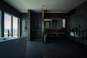a black bathroom with a tub and a large window at eureka awaji 絶景インフィニティプール x 露天温水ジャグジー付きヴィラ in Sumoto