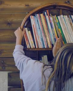 a girl reaching for a book shelf of books at Camping Le Boem in Balazuc