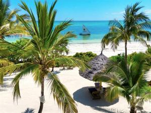 a beach with palm trees and a boat in the water at Kijani Beach Villas in Bwejuu