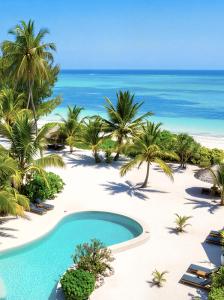 a pool on a beach with palm trees and the ocean at Kijani Beach Villas in Bwejuu