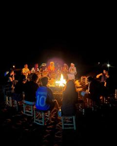 a group of people sitting around a fire at night at Merzouga Luxury Camping in Merzouga