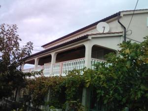 a white house with a balcony and trees at Apartmani Roza Lopar in Lopar