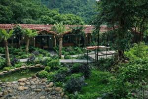 a garden with a house with a pond and palm trees at Trang An Mountain River Ecolodge in Ninh Binh