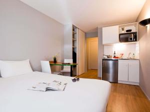 a bedroom with a white bed and a small kitchen at Aparthotel Adagio Access Paris Maisons-Alfort in Maisons-Alfort