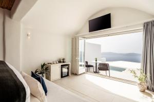 a white bedroom with a large sliding glass door leading to a patio at Rocabella Santorini Hotel & Spa in Imerovigli