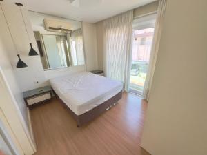 a bedroom with a white bed and a large window at Excelente Apto no condomínio Boulevard in Bombinhas +9 photos