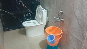 a bathroom with a toilet and an orange bucket at Hotel O V GUEST INN in Bhattiprolu