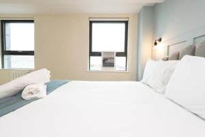 a white bedroom with a large bed and two windows at The Swansea Central Hall 1 Bed Room Apartment in Swansea