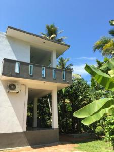 a building with a balcony with palm trees on top at Belgi Guest House in Balapitiya