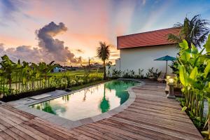 a pool with a wooden deck next to a house at Svadarma Bali Villa by Dhananjaya Hospitality in Darmasaba