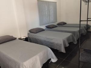 three beds in a room with white sheets at Espaço Ideal 7 in Cascavel