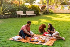 a man and a woman and a dog sitting on a picnic blanket at SaffronStays Eden - 3BR vineyard-side pool villa with jacuzzi, farm dining, stargazing deck & lawns for celebrations in Nashik