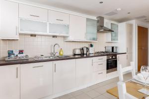 a white kitchen with white cabinets and appliances at A Wave From It All - Extensive Harbour Views from Wrap-Around Balcony in Poole