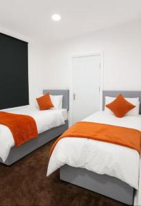 two beds with orange and white sheets in a bedroom at Lincoln Manor 5BR in Peterborough
