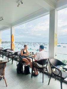two people sitting at tables in a restaurant looking out at the water at Bay View Resort & Villas Mũi Né in Phan Thiet