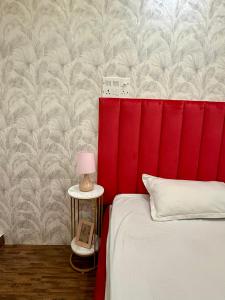 a bed with a red headboard and a table with a lamp at Cutesy space in Kolkata