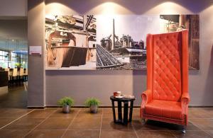 a red chair in a lobby with a picture on the wall at Leonardo Hotel Völklingen-Saarbrücken in Völklingen