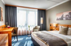 a hotel room with a bed and a desk and window at Leonardo Hotel Köln Bonn Airport in Cologne