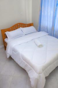 a white bed with a wooden headboard and white sheets at Aurora Loisse Suites in Nakuru