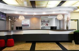 a lobby with a reception desk with red chairs at Leonardo Hotel Munich Arabellapark in Munich