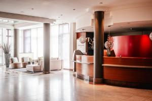 a lobby of a hotel with a red counter and chairs at Leonardo Hotel Aachen in Aachen