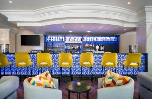 a bar in a hotel with yellow chairs and a counter at Leonardo Hotel Düsseldorf City Center in Düsseldorf