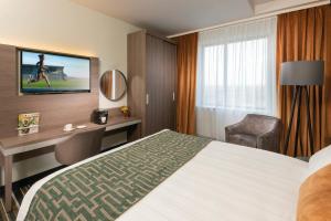 a hotel room with a bed and a desk and a television at Leonardo Royal Hotel Amsterdam in Amsterdam