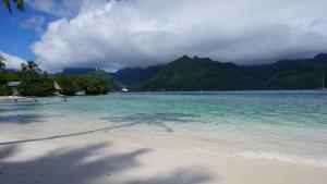 a beach with people in the water and mountains at MOOREA - Coconut Pool House 4 in Pihaena