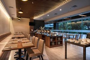 ジャカルタにあるGrand Whiz Poins Simatupang Jakartaの木製のテーブルと椅子、大きな窓のあるレストランを併設しています。