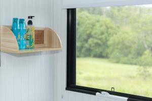 a window sill with bottles on a shelf next to a window at Hill Creek Tiny House 5 by Tiny Away in Perwillowen