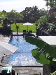 a swimming pool with an umbrella and a table and chairs at Sri Aksata Ubud Resort in Ubud