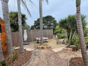 a patio with a table and a fence and palm trees at Cedar Hill Retreat in Venus Bay