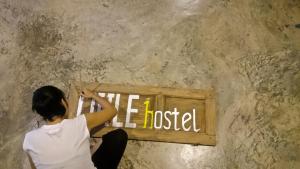 Una donna è seduta su un cartello su un muro di Little Hostel a Ban Houayxay