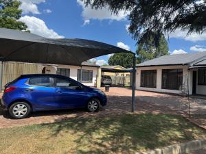 a blue car parked under an umbrella in front of a house at No7 Mc Intyre Guest House in Sasolburg