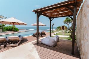 a wooden deck with chairs and umbrellas and the ocean at Nalas Villa in Ketewel