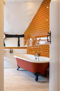 a red tub in a bathroom with a brick wall at The Richard Onslow in Cranleigh