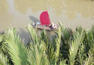 a person on a boat with a red umbrella in the water at Comfy room - InnerZen Mekong Riverside homestay Ben Tre in Ben Tre