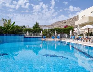 a large blue swimming pool with chairs and a building at Lindos Athena in Lindos