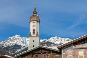 a clock tower on top of a building with snow covered mountains at Ferienwohnung Kramerblick Marienplatz in Garmisch-Partenkirchen