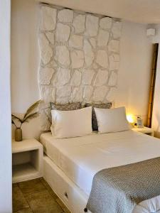 a bedroom with a white bed with a stone wall at Jemphasis-New Apartments Mykonos in Agios Ioannis Mykonos