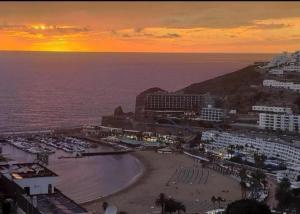 a sunset over a beach with a resort and the ocean at New Puerto Rico Terrace Swiming Pool in Mogán