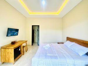 a bedroom with a bed and a desk and a television at Umah Kak Pasek in Jimbaran