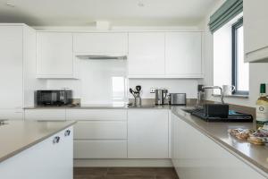 a white kitchen with white cabinets and appliances at Beachcliff - On the Seafront with Two Balconies in Bournemouth
