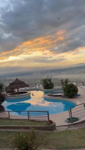 a group of swimming pools with a sunset in the background at ERNESTINA VILLAGE Resort Apart & suites in Villa Carlos Paz