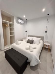 a white bedroom with a large bed with a black ottoman at One Apartamentos in Torreorgaz