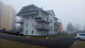 a white building with balconies and a car parked in a parking lot at Apartment Kliniknähe in Idar-Oberstein