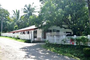 a white house with a fence next to a road at Upali Homestay in Kandy