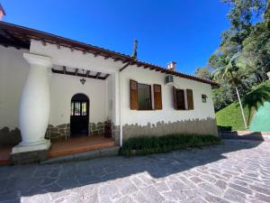 a white house with a black door and trees at Casa Vale da Serra - Petrópolis in Petrópolis
